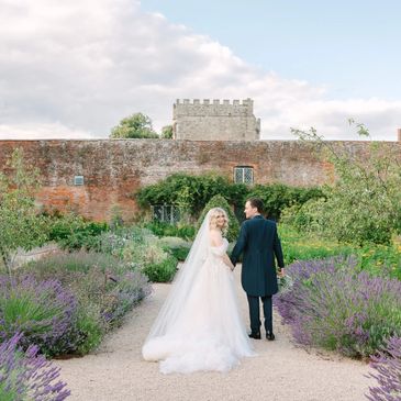 Bride and groom walking hand in hand in a garden path beside lavender.