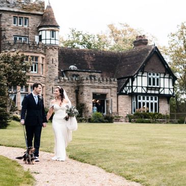 Newlywed couple walking with their dog outside a historic mansion.