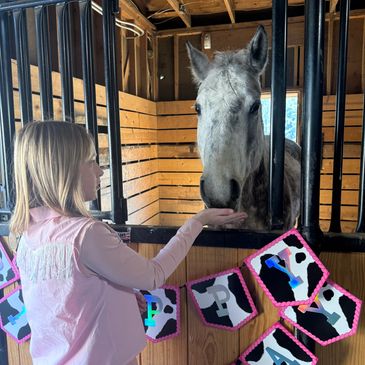 A girl feeding a gray horse inside a wooden stable.