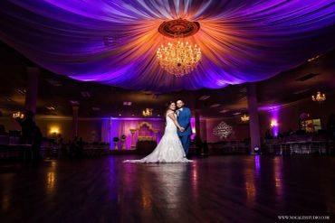 Bride and groom dancing under elegant purple and orange lighting.