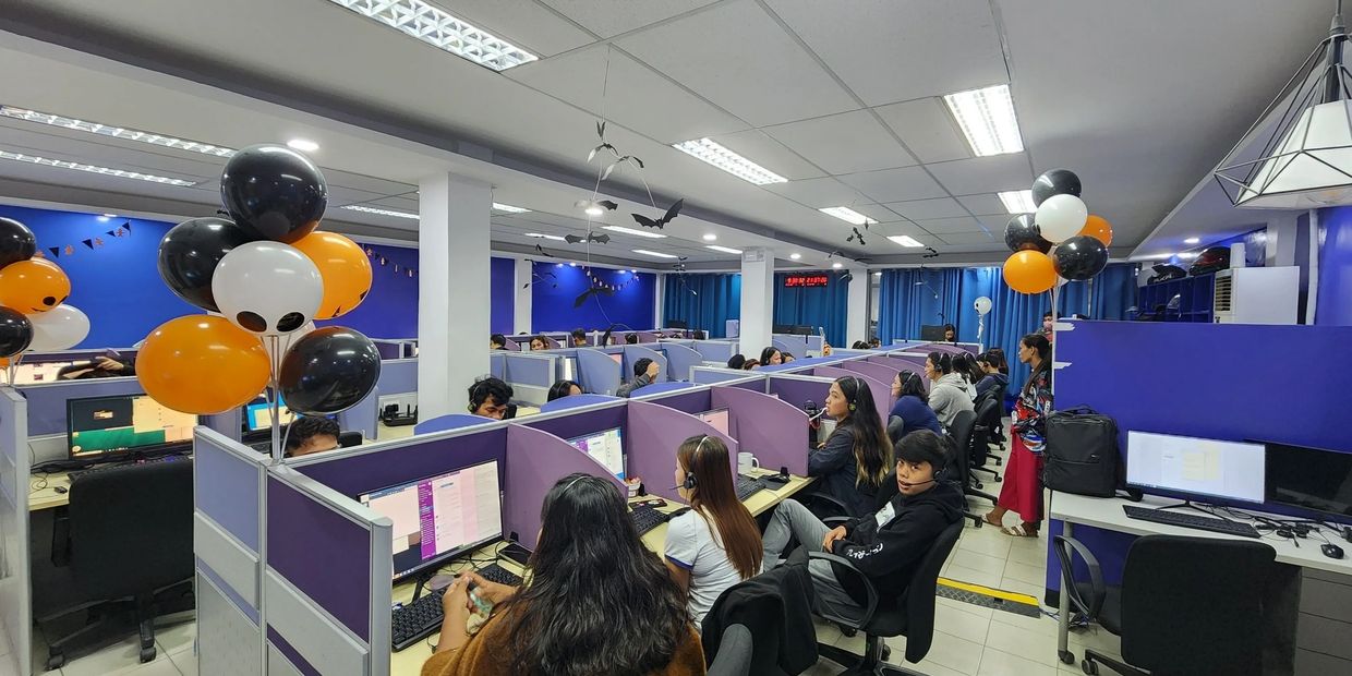 Call center decorated with Halloween balloons and bats, employees working at desks.