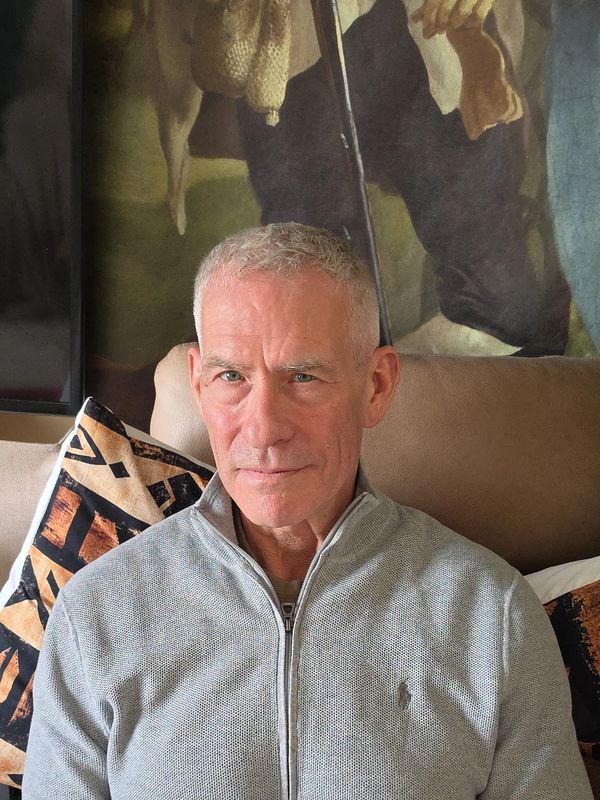 Mature man with gray hair in a light gray zip-up sweater sitting on a couch.