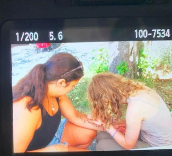 Two women creating a henna tattoo outdoors.
