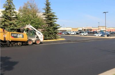 Roadwork paving fresh asphalt in a parking lot near shopping stores.