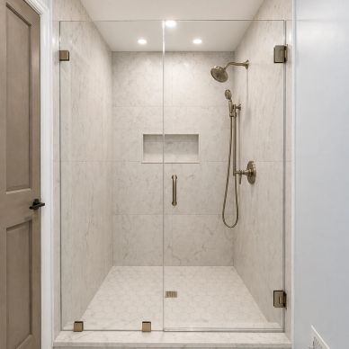 Modern glass shower with brass fixtures and marble walls.
