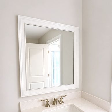 White-framed mirror above a bathroom sink with brass faucet.