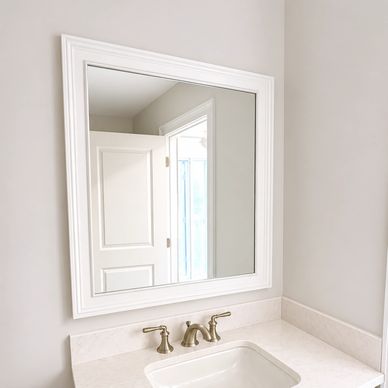 White-framed mirror above a bathroom sink with brass faucet.