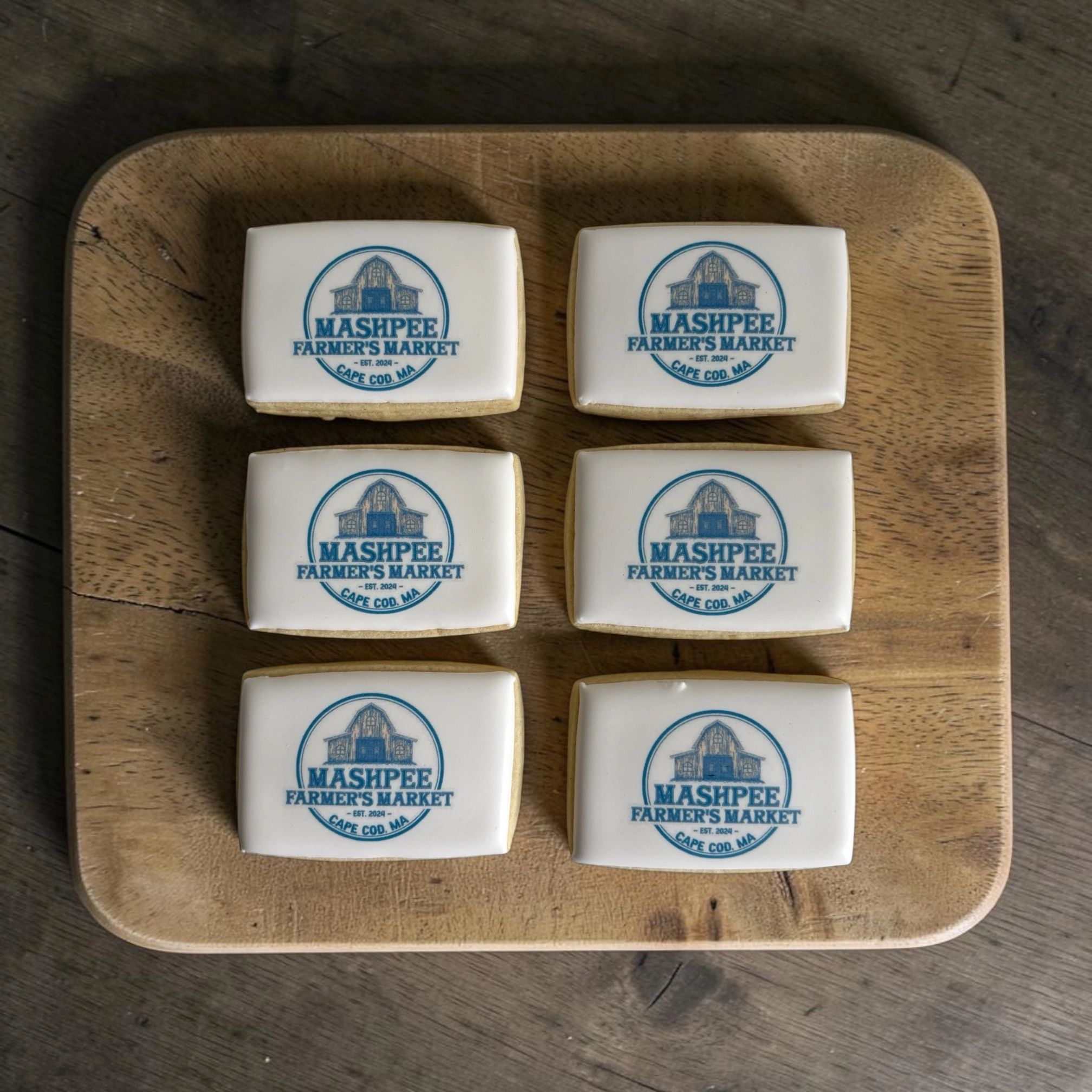 Cookies with Mashpee Farmer's Market logo on a wooden board.
