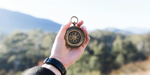 Hand holding a vintage compass outdoors with mountains in the background.