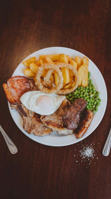 A hearty meal with egg, fries, onion rings, peas, meats on a white plate.