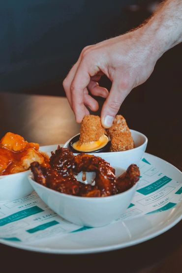 Hand dipping a fried snack into sauce with bowls of wings and other appetizers.