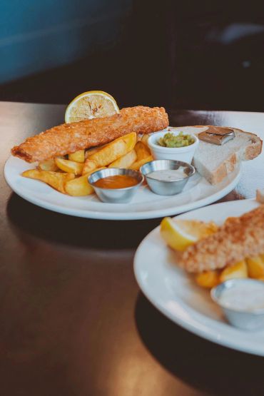 Classic fish and chips served with sauces, bread, and lemon wedge.