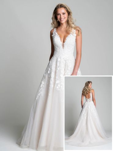 Smiling woman modeling a white lace wedding dress with a deep V neckline and flowing skirt.