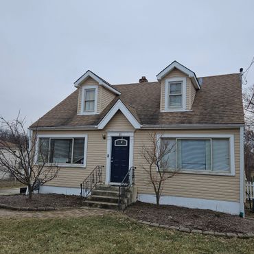 Small beige house with blue front door and two dormer windows.