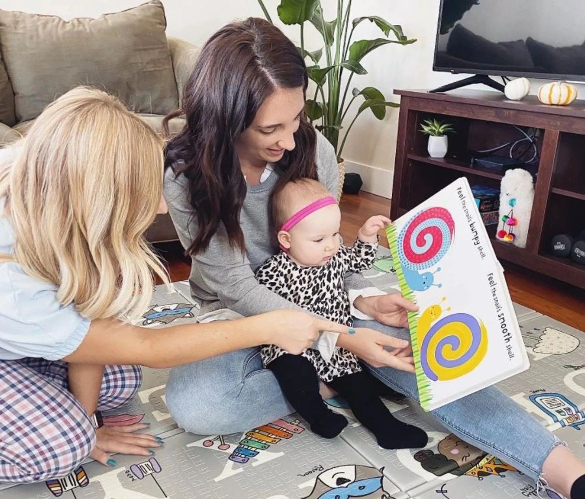 Speech therapist sitting in a home session with a mother and infant reading a book