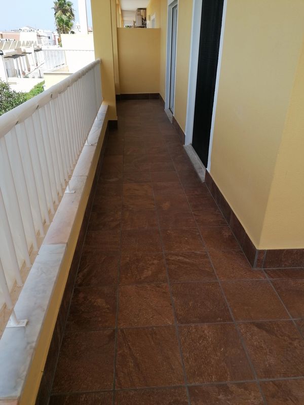 Sunny apartment balcony with tile flooring and white railing.