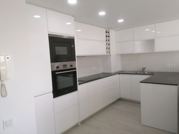 Modern white kitchen with built-in appliances and wine rack.