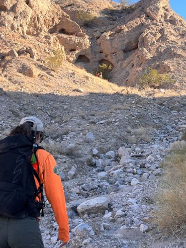 Hiker approaching rocky caves in a desert landscape.