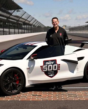 Man standing next to a white sports car with Indy 500 logo.