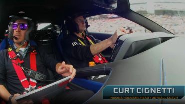 Two men in a car, one with a headset and clipboard.