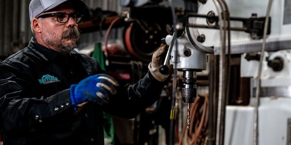 Worker using industrial drill press for metal fabrication