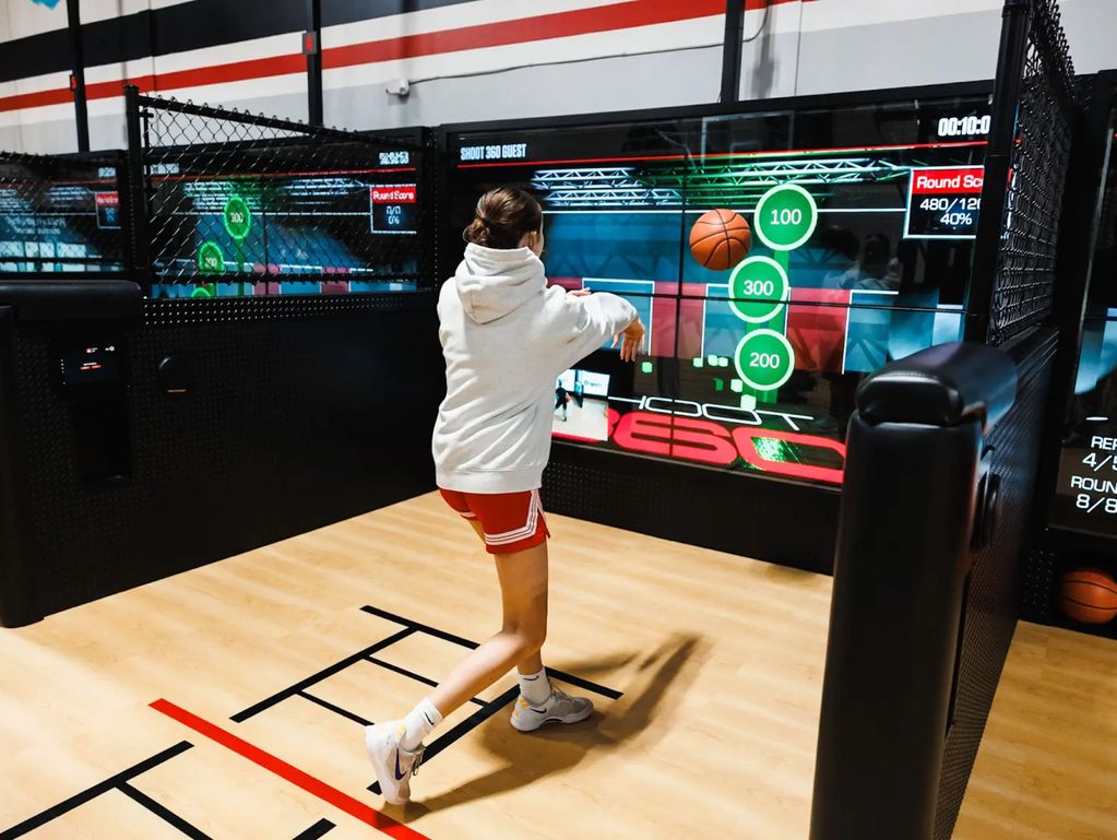 Person playing virtual basketball shooting game indoors.