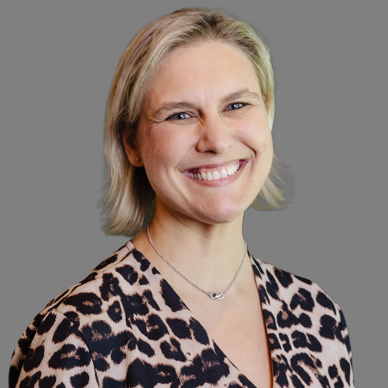 Smiling woman in leopard print blouse with short blonde hair and silver infinity necklace.