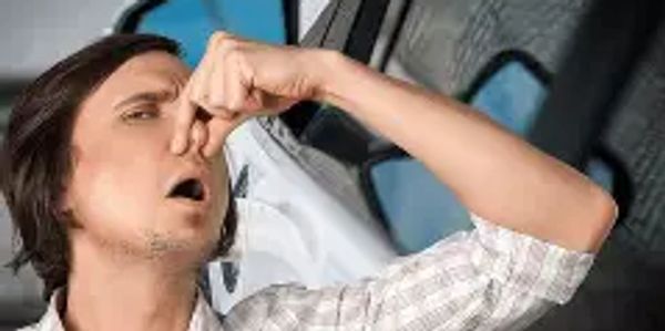 Man holding his nose near a car, indicating a bad smell.