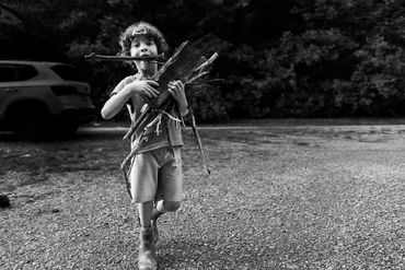 documentary photography- boy carries sticks in mouth