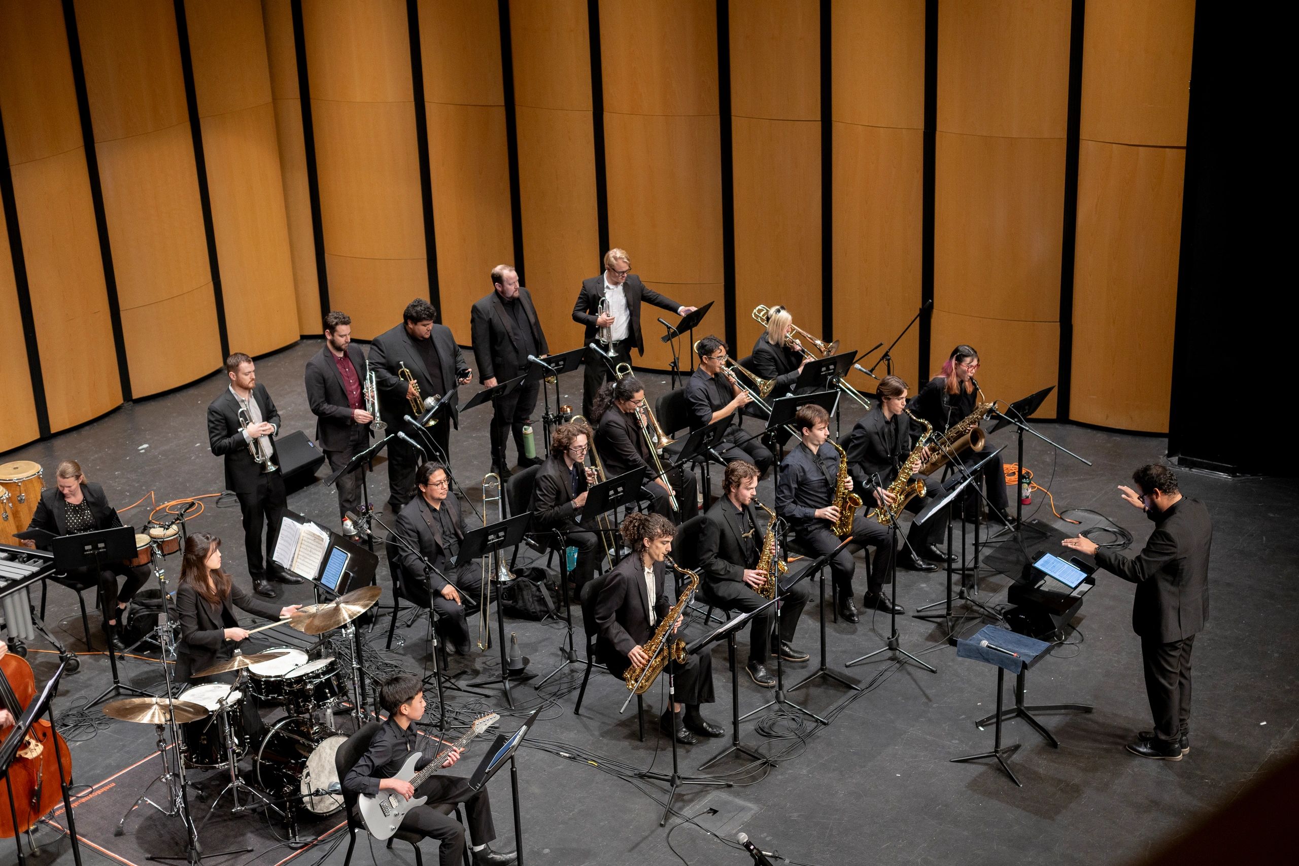 A jazz band performs on stage with a conductor leading them.