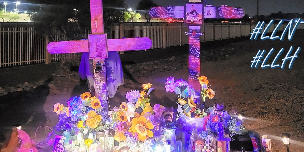 Nighttime memorial with crosses, flowers, and lights honoring loved ones.