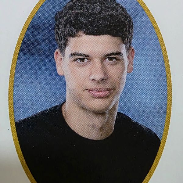 Young man with short curly hair in a portrait photo with a blue background.