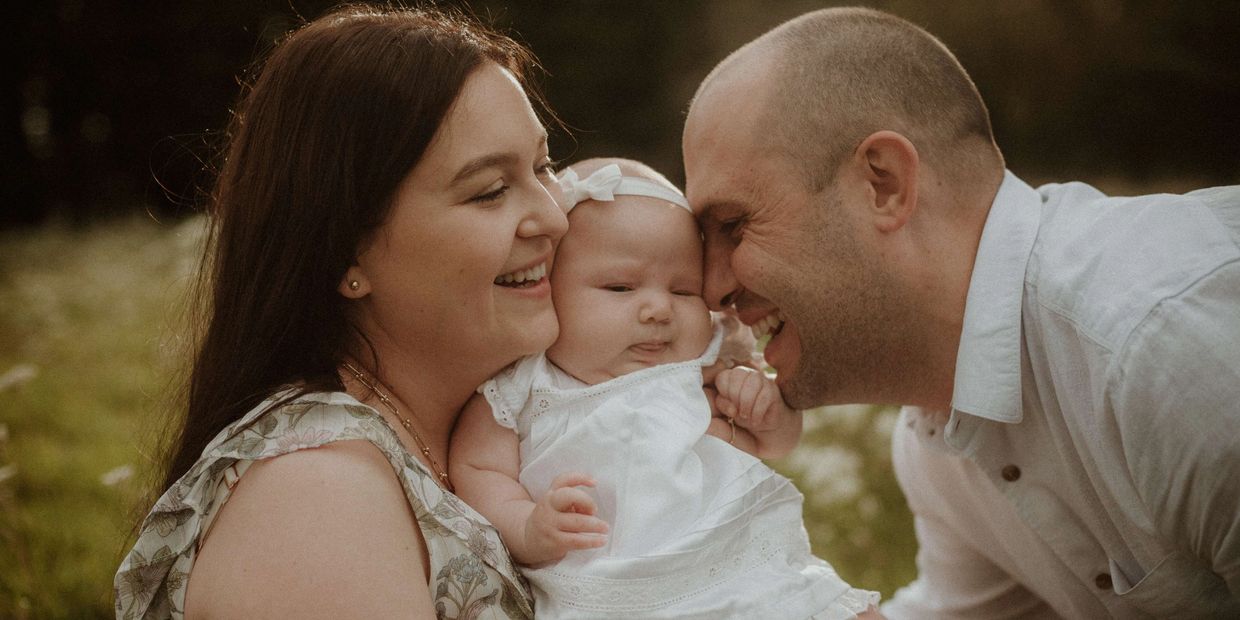 Parents happily holding their baby outdoors.