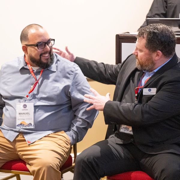Two men with name tags engage in a friendly conversation during a conference.