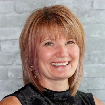 Smiling woman with short blonde hair against a gray brick wall.