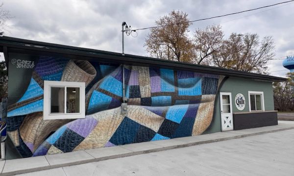 Mural de un patrón de colcha en tonos azules y morados en la pared de un edificio.