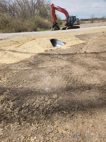 Excavator near a dirt area with a culvert pipe installation.