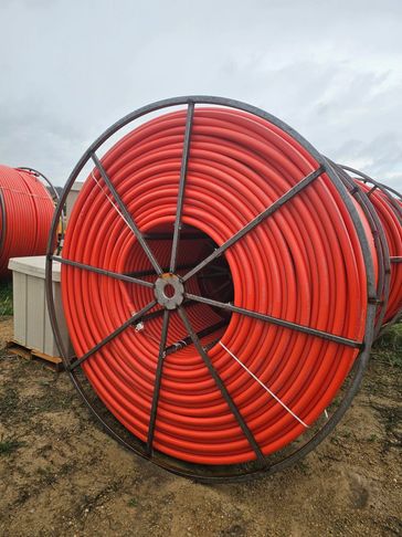 Large coil of orange tubing or pipe on a metal reel outdoors.