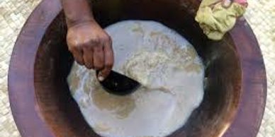 Hand stirring a thick mixture in a large wooden bowl.
