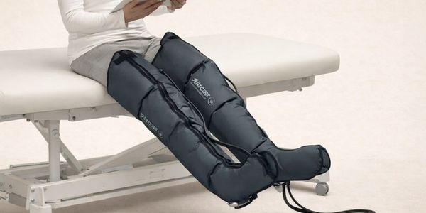 Person using black leg compression sleeves while seated on a medical table.