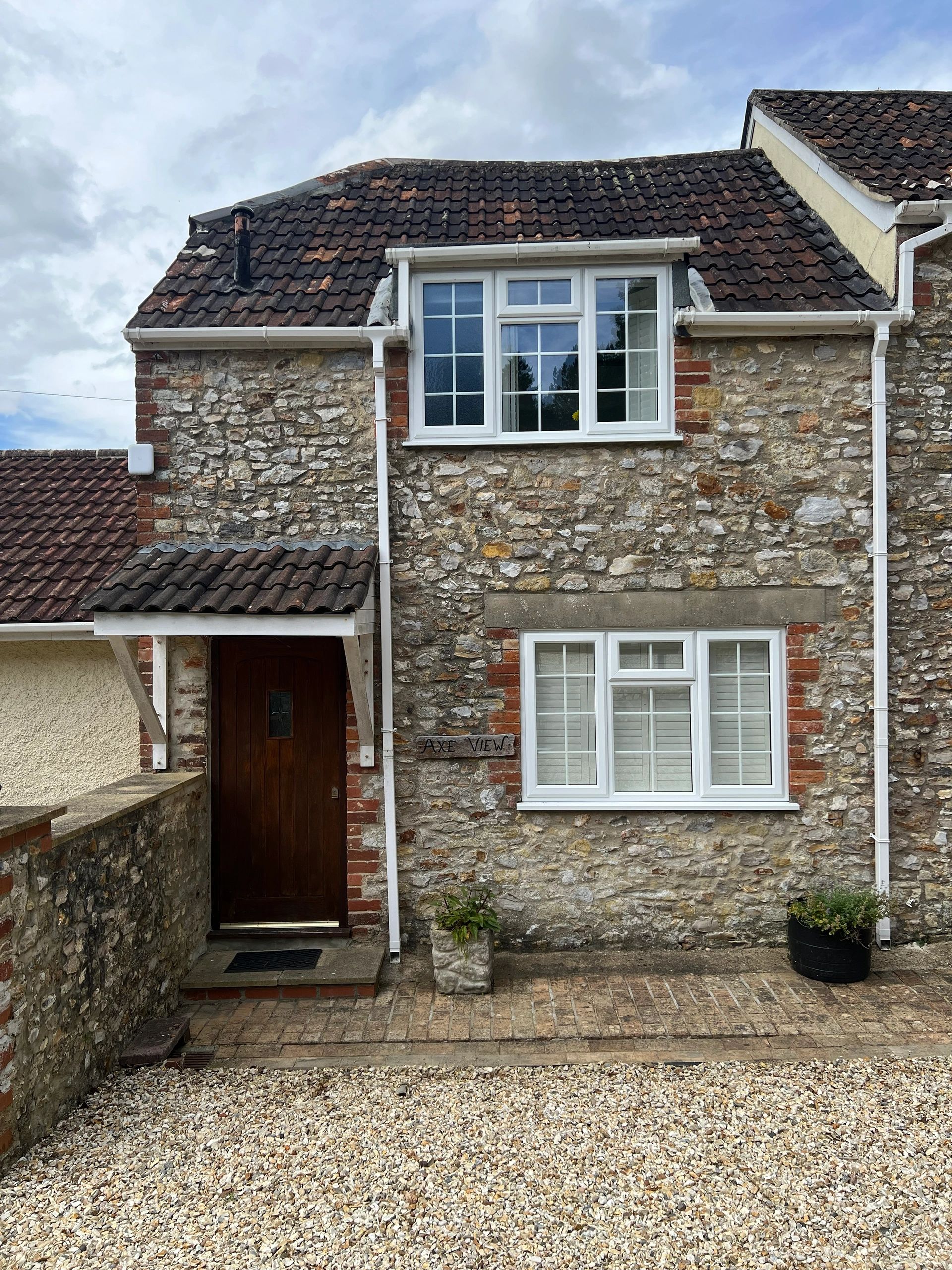 Stone cottage with white windows and a gravel driveway.