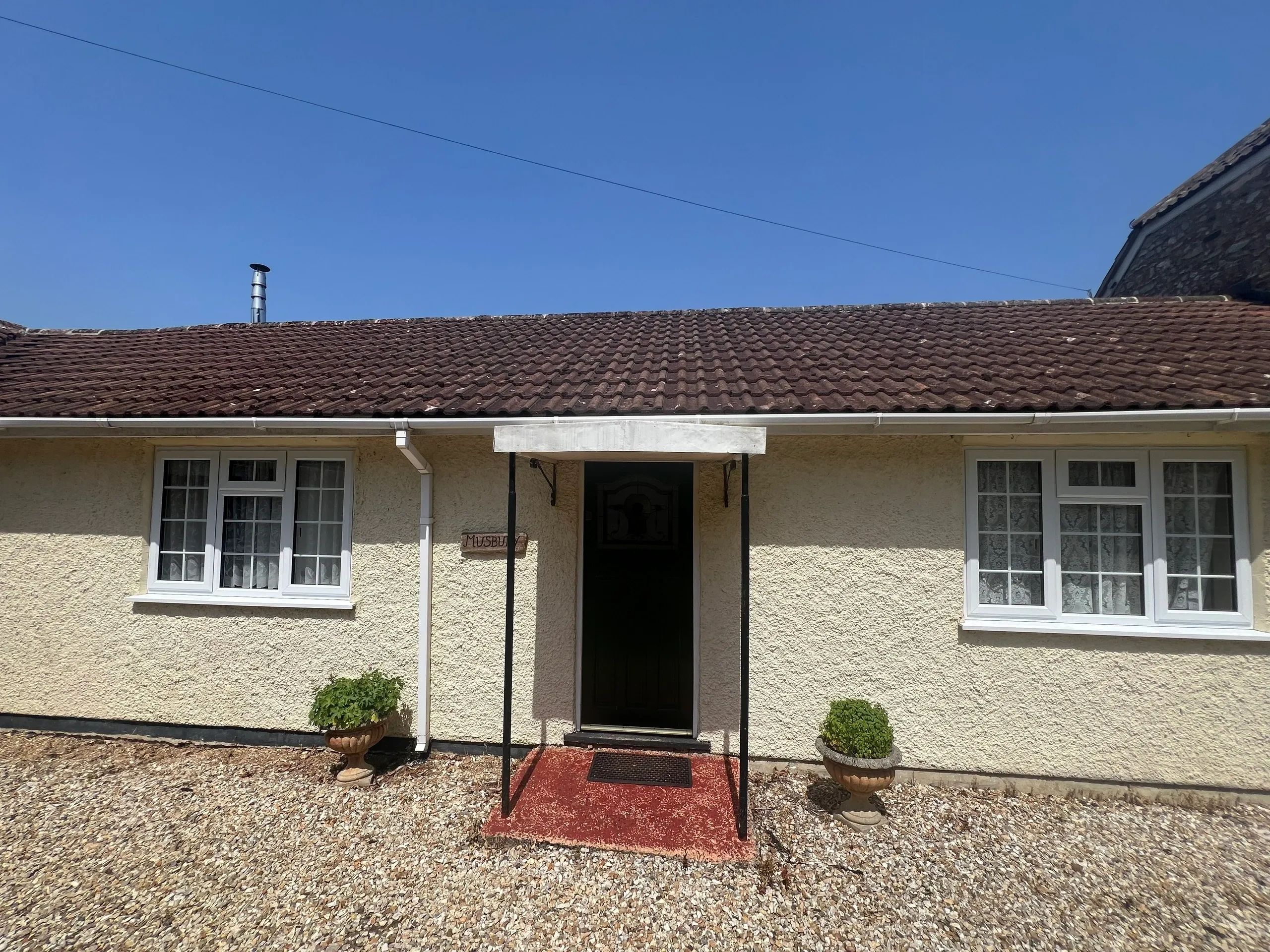 Front entrance of a beige house with two windows and potted plants.
