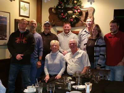 A group of eight people smiling in a cozy restaurant with holiday decorations.