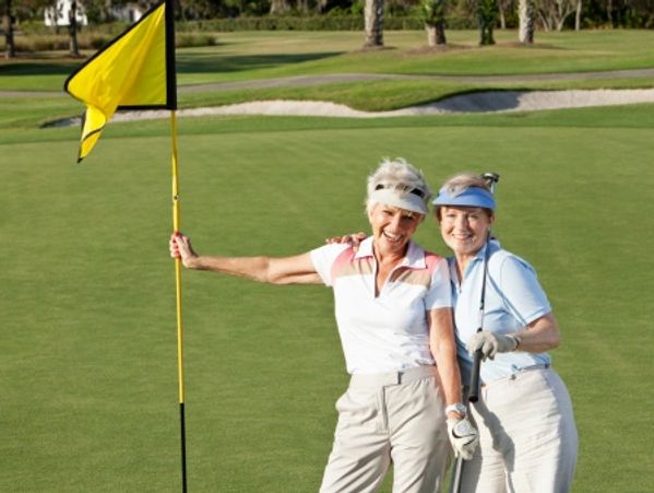 Two smiling women posing on a golf course green.
