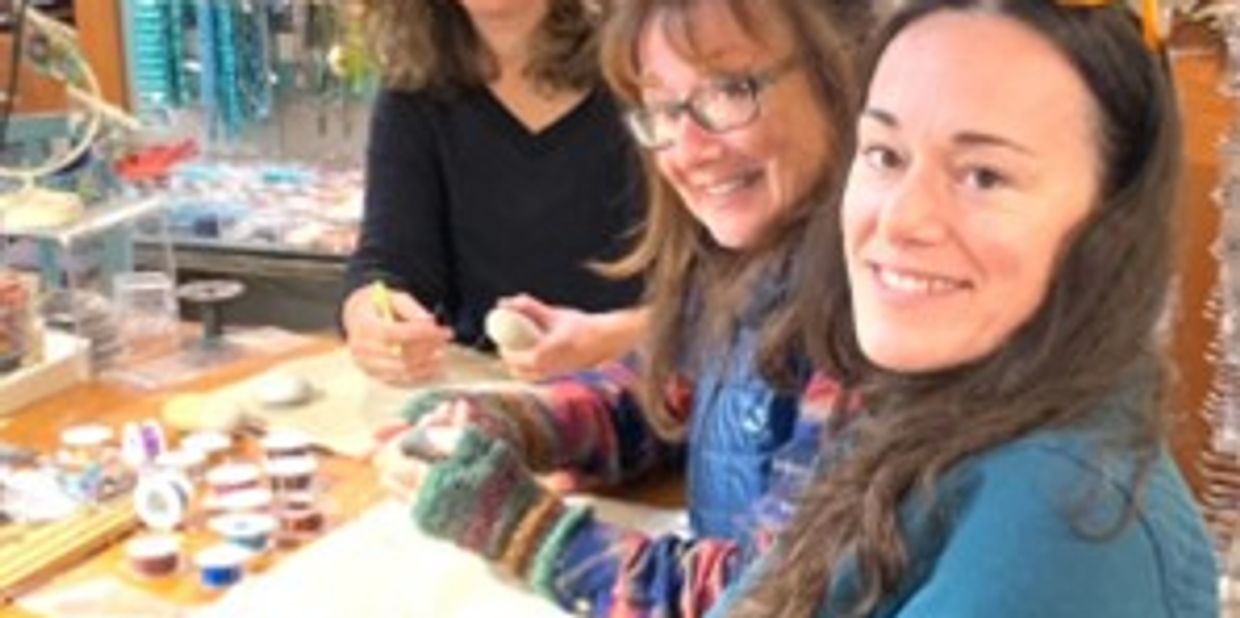 Three women crafting together at a table filled with art supplies.