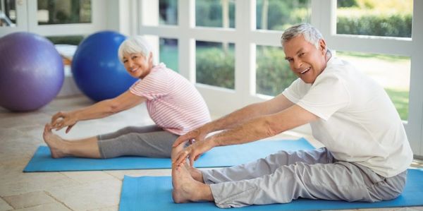 Older couple stretching on yoga mats indoors.