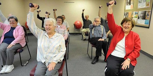 Seniors exercising with dumbbells in a seated class.