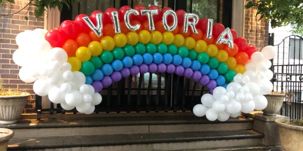 Colorful rainbow balloon arch with the name Victoria in silver letters.