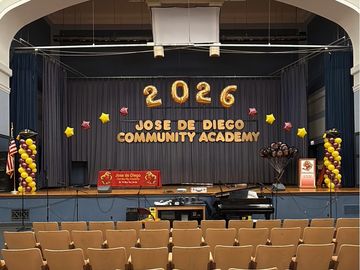 A decorated school stage with 2026 balloons and community academy name.