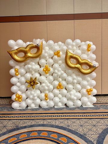 White and gold balloon backdrop with masquerade masks for event decor.